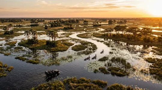 Safari vehicles and boats navigating flooded plains during peak water season in African wilderness