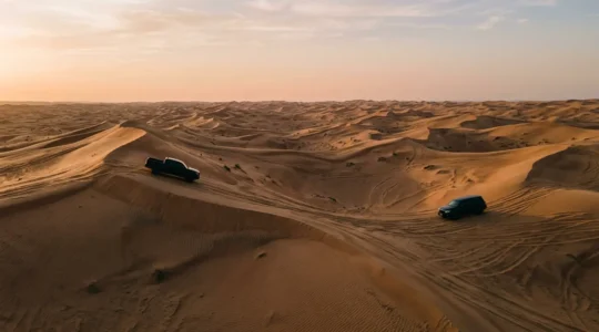 Toyota Hilux and Land Cruiser crossing deep sand dunes in dramatic golden hour lighting