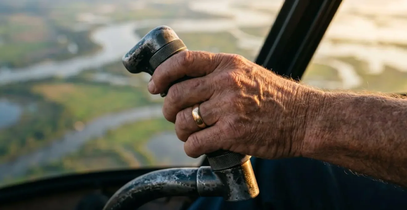 Close-up macro view of weathered pilot hands on helicopter controls with delta landscape reflection