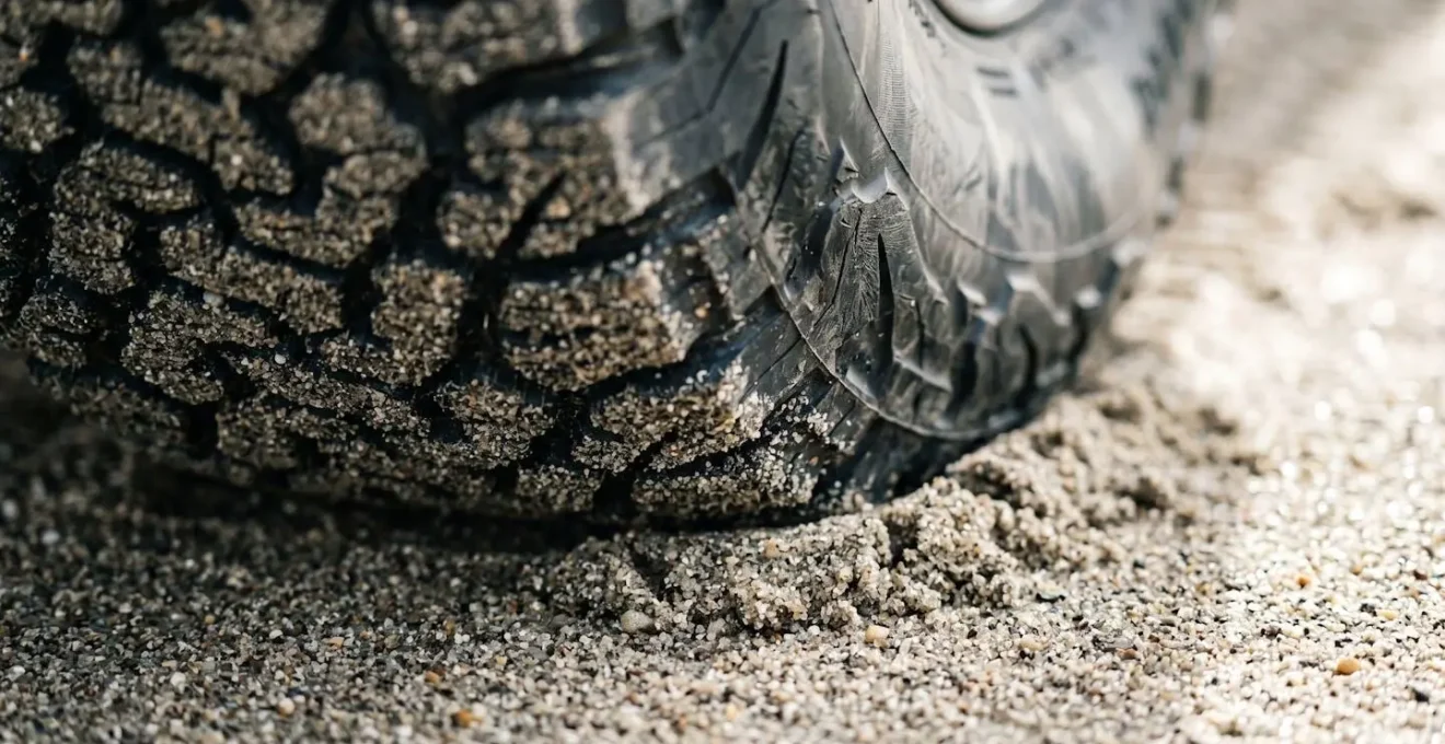Macro view of tire sidewall bulge and elongated footprint of a 4x4 tire in sand, demonstrating the principle of flotation.